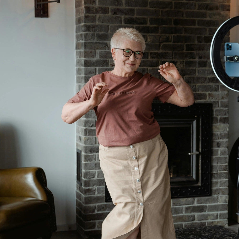 Person in a pink shirt and beige pants standing in a room with a brick wall and a lamp.
