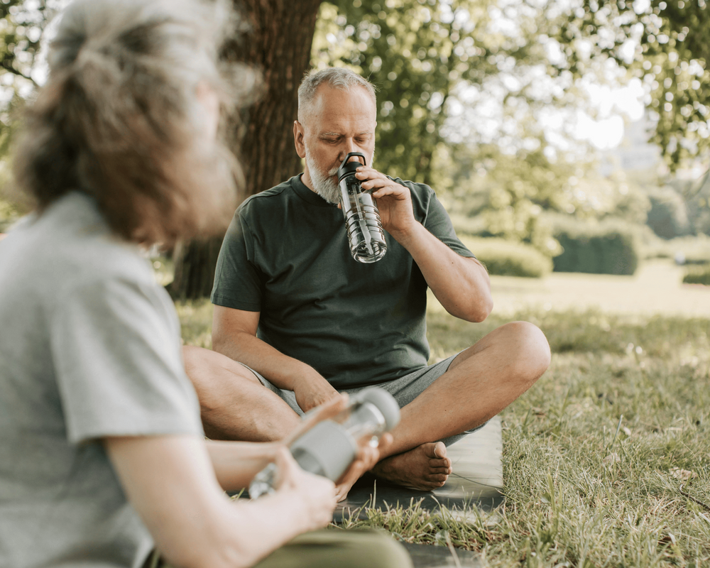 Two people sitting on grass outdoors, one drinking from a water bottle.
