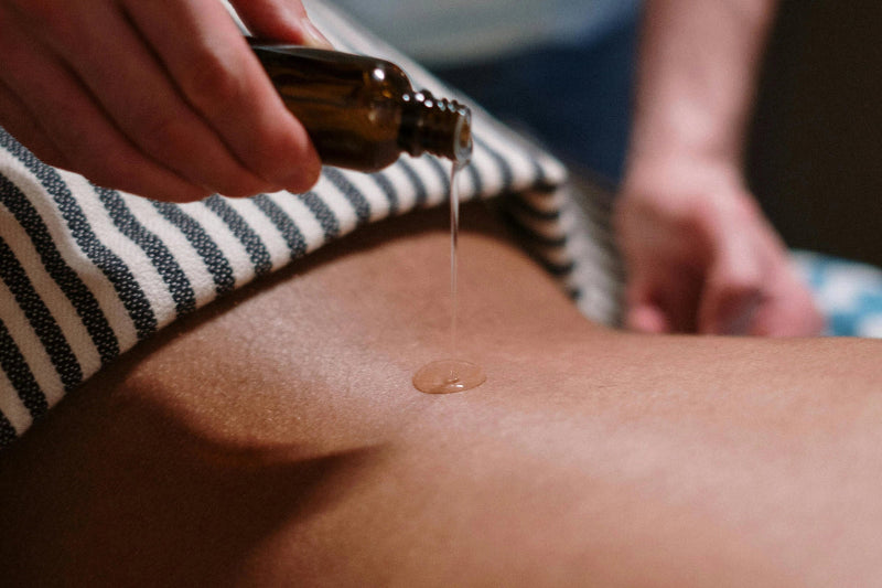Person applying oil to a person's skin with a small bottle.