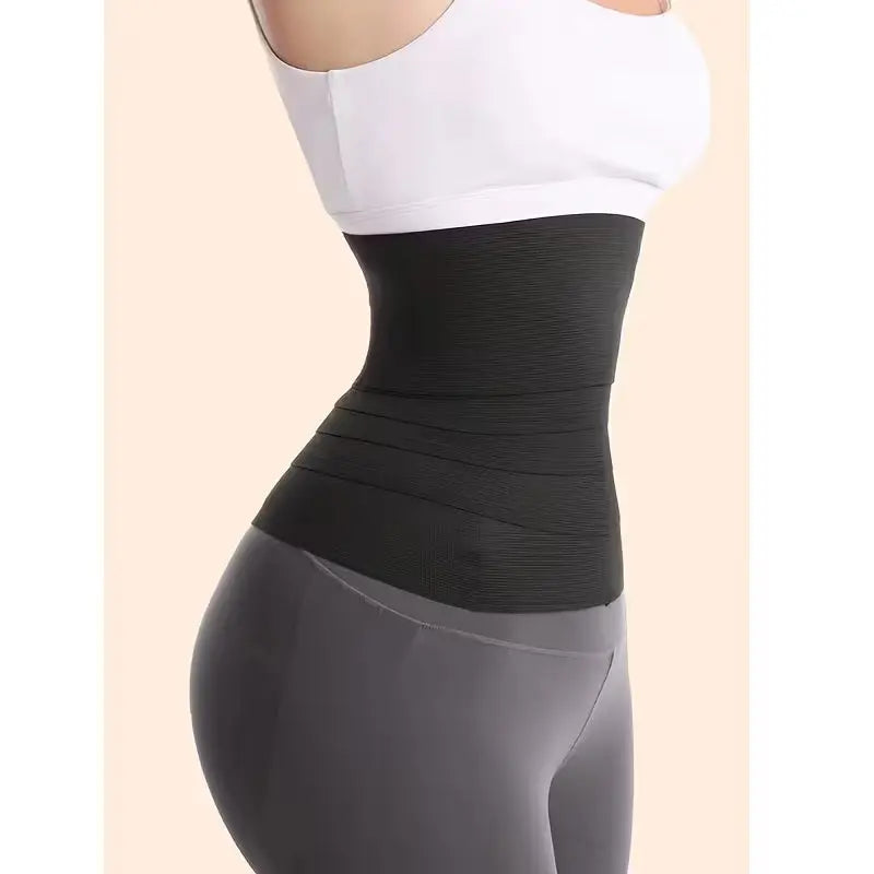 Person wearing a black waist trainer with a white sports bra and gray leggings on a beige background